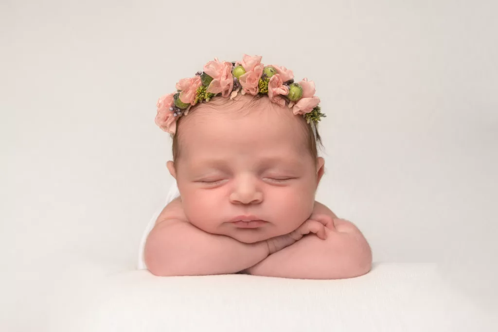 Photographie de bébé endormi et portant une couronne de fleurs.