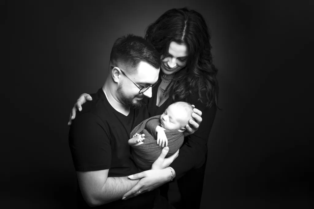 Photo noir et blanc de parents tenant dans leur bras un nouveau né.