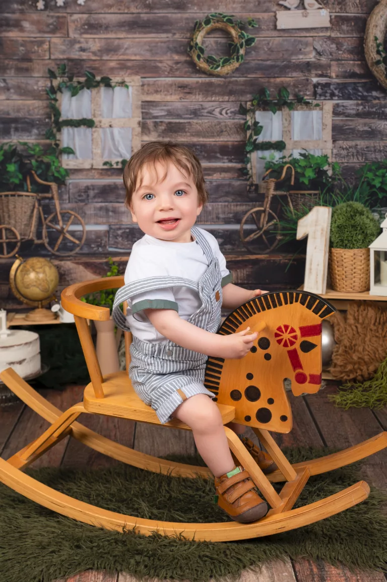 Bébé de 1 an fêtant son 1er anniversaire lors d'une séance chez le photographe. Il est sur un cheval de bois avec un grand sourire.