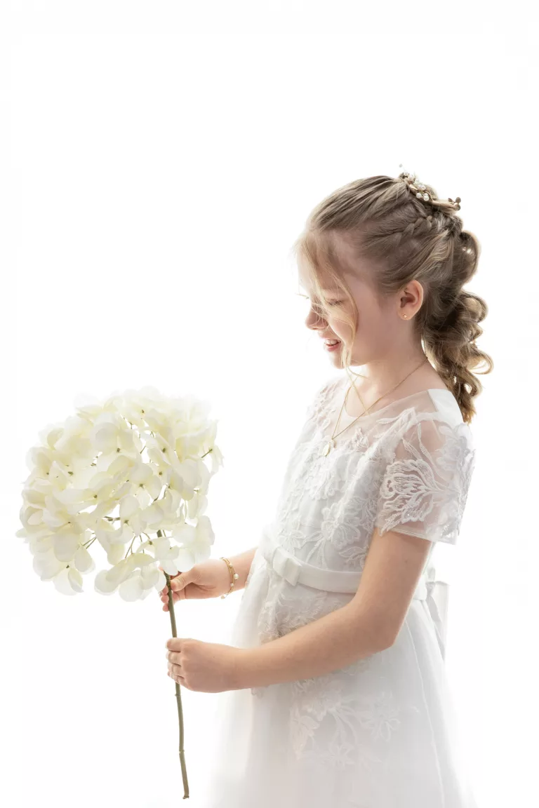 jeune fille en tenue de communiante, regardant une grosse fleurs qu'elle tient dans les mains